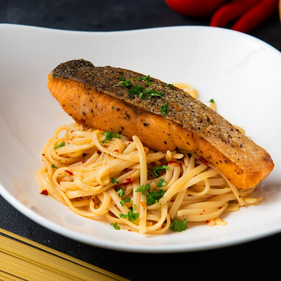 Crispy-skinned salmon fillet atop a bed of linguine pasta with red pepper flakes and parsley.