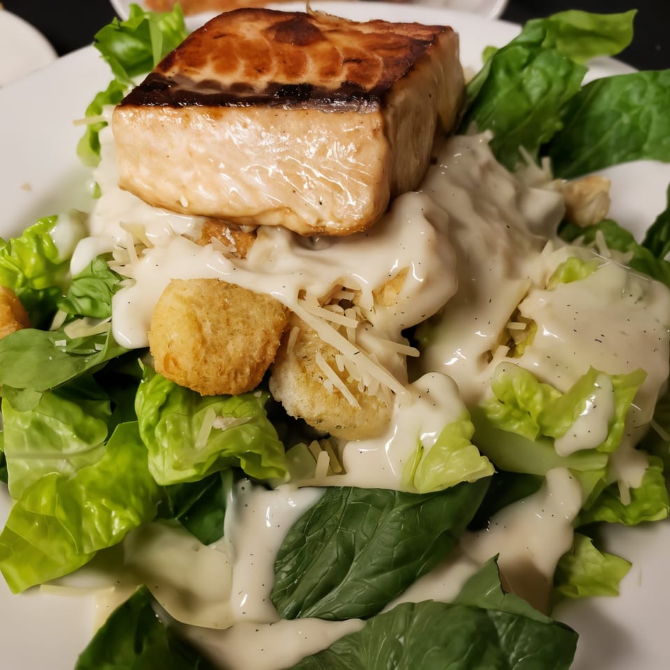 Grilled salmon fillet atop a Caesar salad with croutons, parmesan, and creamy dressing.